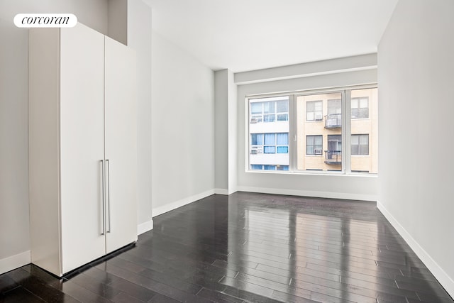 empty room with dark wood-type flooring and baseboards