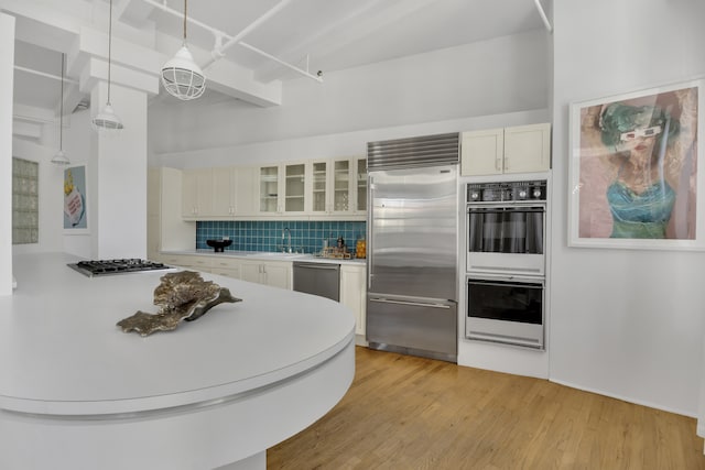 kitchen featuring stainless steel appliances, tasteful backsplash, light countertops, light wood-style flooring, and glass insert cabinets