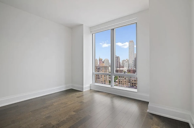 spare room with plenty of natural light, baseboards, a city view, and dark wood-style flooring