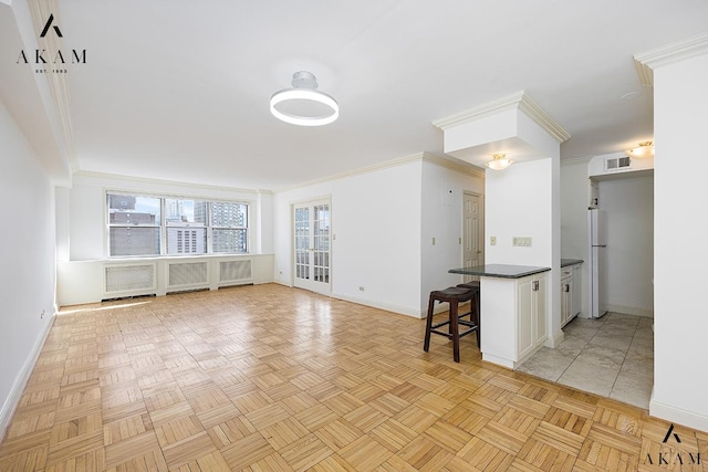 kitchen featuring crown molding, dark countertops, freestanding refrigerator, a kitchen breakfast bar, and baseboards