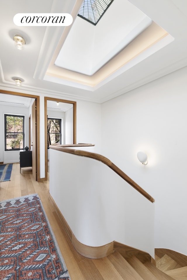 hall with a tray ceiling, an upstairs landing, baseboards, and light wood finished floors