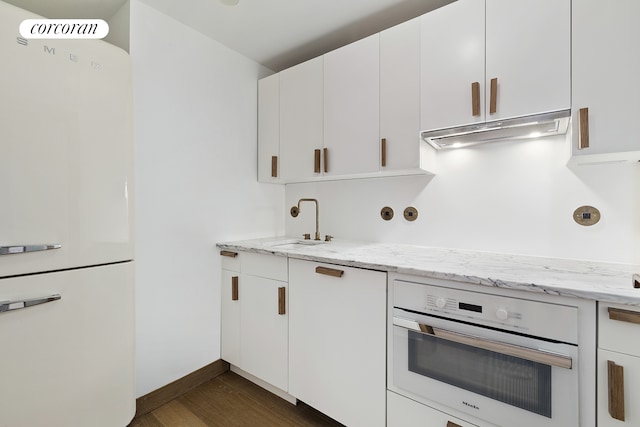 kitchen with white appliances, light stone counters, dark wood-style floors, a sink, and white cabinetry