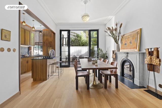 dining room featuring crown molding, a fireplace with flush hearth, and light wood-style floors