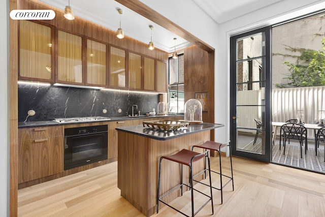 kitchen featuring a kitchen breakfast bar, stainless steel gas stovetop, dark countertops, black oven, and brown cabinets