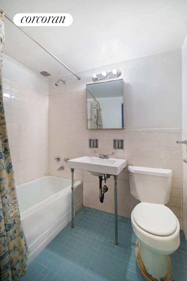 bathroom featuring shower / bathtub combination with curtain, toilet, tile walls, wainscoting, and tile patterned flooring