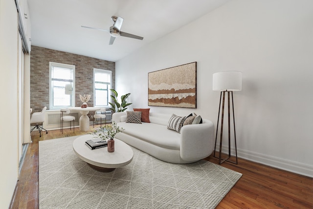 living room featuring baseboards, a ceiling fan, wood finished floors, and brick wall