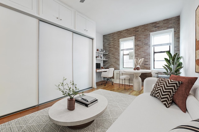 living area with brick wall, built in study area, and wood finished floors