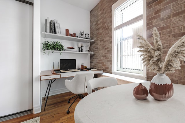 home office with wood finished floors and brick wall