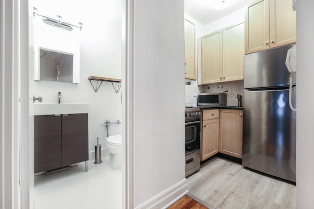 kitchen featuring dark countertops, a sink, light wood-style flooring, backsplash, and stainless steel appliances