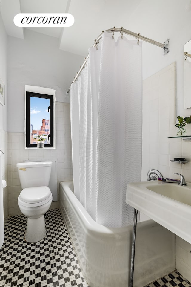 bathroom with toilet, a sink, tile walls, and shower / tub combo with curtain