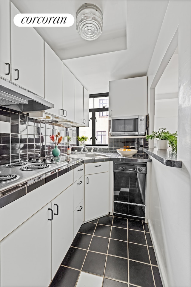 kitchen with appliances with stainless steel finishes, backsplash, white cabinetry, and under cabinet range hood