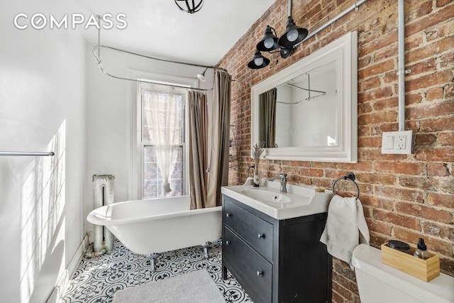 bathroom with a freestanding bath, brick wall, vanity, and toilet