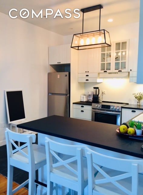 kitchen featuring dark countertops, glass insert cabinets, a kitchen breakfast bar, stainless steel appliances, and white cabinetry