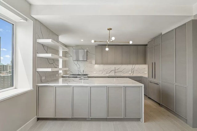 kitchen with gray cabinetry, a peninsula, a sink, light stone countertops, and open shelves