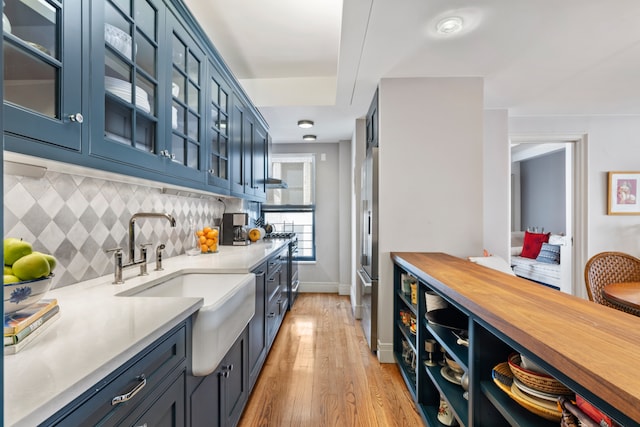 kitchen with tasteful backsplash, light wood-style floors, glass insert cabinets, a sink, and baseboards