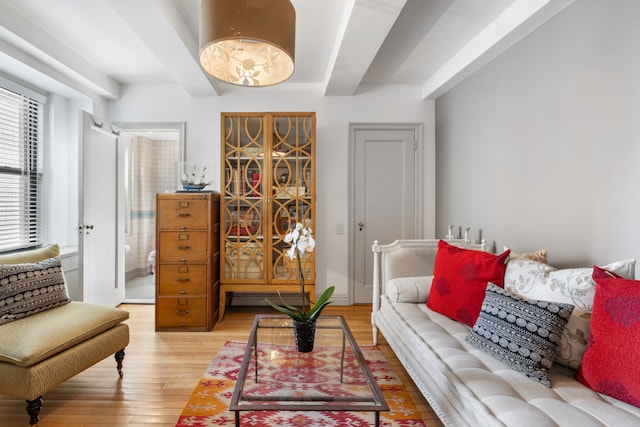 living area with baseboards, beamed ceiling, and light wood-style floors