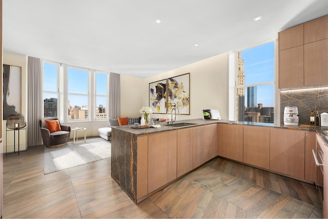 kitchen featuring a city view, tasteful backsplash, dark countertops, a sink, and a peninsula