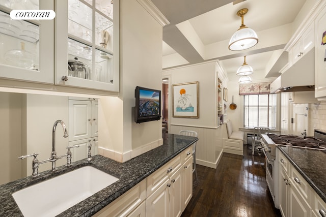 kitchen featuring stainless steel stove, a sink, wainscoting, dark stone counters, and dark wood finished floors