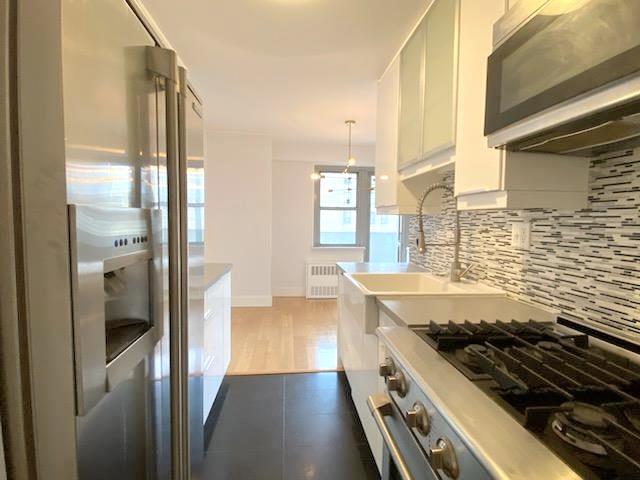 kitchen with radiator, decorative backsplash, stainless steel gas range oven, white cabinetry, and refrigerator with ice dispenser