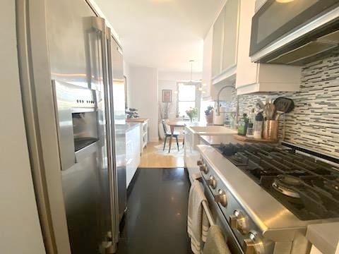 kitchen featuring decorative backsplash, premium appliances, white cabinetry, and a sink