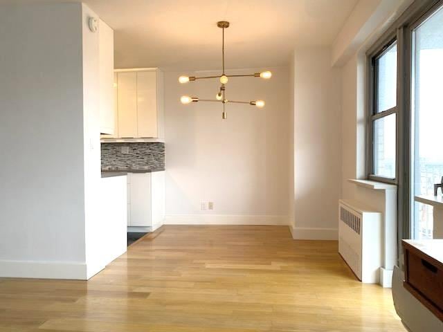 unfurnished dining area with a notable chandelier, radiator heating unit, light wood-style floors, and baseboards