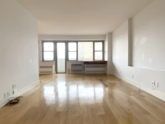 spare room featuring radiator, a wall mounted AC, baseboards, and wood finished floors