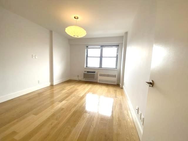 unfurnished room featuring light wood-style flooring, radiator, and baseboards