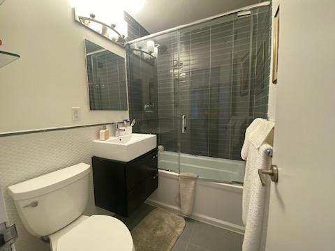 bathroom with tile patterned floors, toilet, vanity, and shower / bath combination with glass door