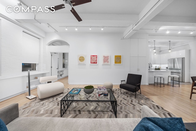 living area featuring rail lighting, arched walkways, light wood-type flooring, and ceiling fan