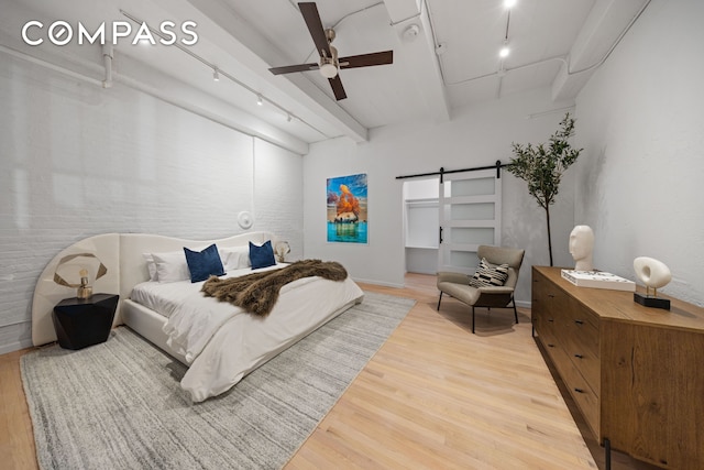 bedroom featuring beamed ceiling, light wood-style flooring, a ceiling fan, a barn door, and rail lighting