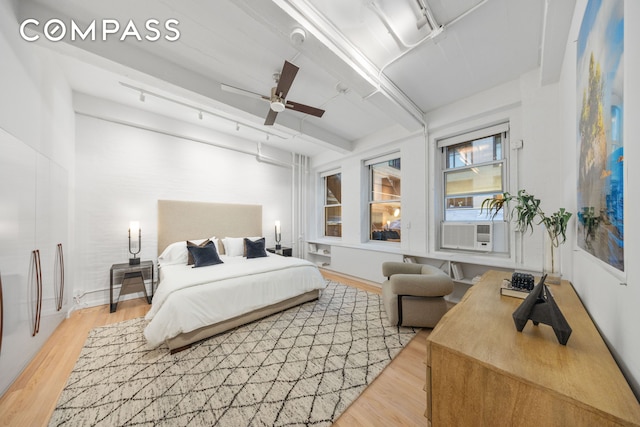 bedroom featuring light wood finished floors, beamed ceiling, rail lighting, and a ceiling fan