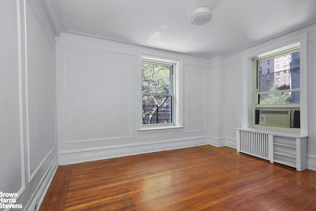 spare room with cooling unit, radiator, a decorative wall, and wood-type flooring