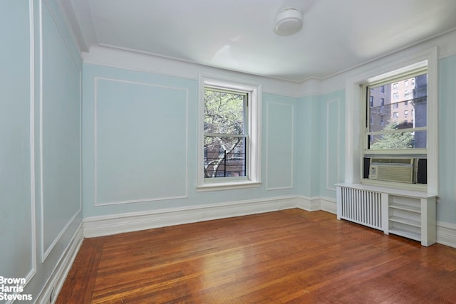 unfurnished room with wood finished floors, radiator heating unit, cooling unit, and a decorative wall