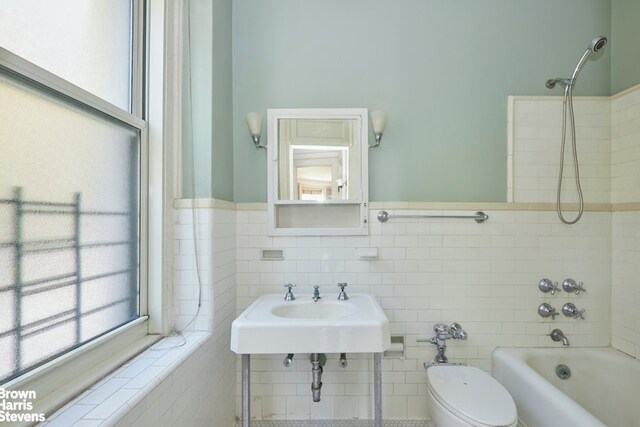 full bathroom with toilet, a sink, washtub / shower combination, and tile walls