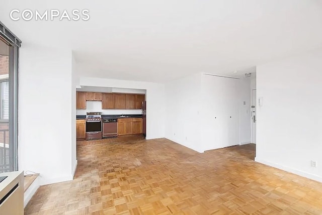 interior space featuring a sink, open floor plan, brown cabinetry, dishwashing machine, and stainless steel range with gas stovetop