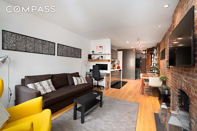 living area with light wood-style floors, brick wall, a brick fireplace, and recessed lighting