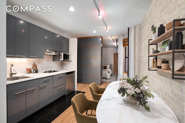 kitchen with stainless steel appliances, gray cabinetry, under cabinet range hood, open shelves, and a sink