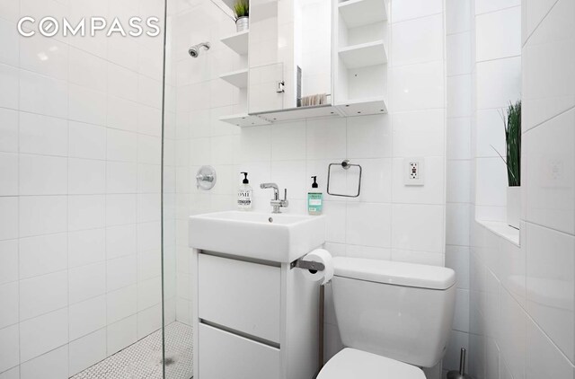 bathroom with toilet, a tile shower, tile walls, and vanity