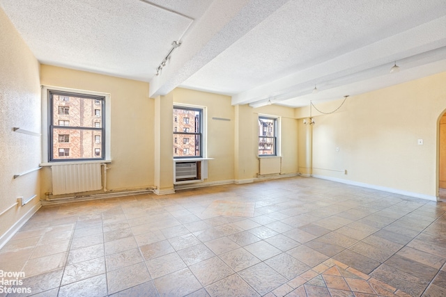 spare room with baseboards, arched walkways, radiator, a textured ceiling, and track lighting