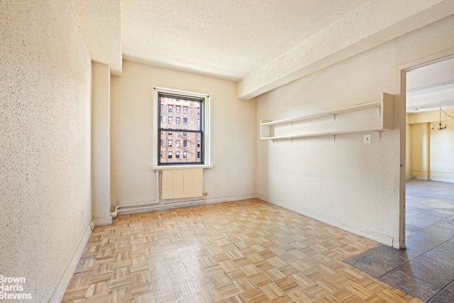 spare room with a textured ceiling, a textured wall, radiator heating unit, and baseboards