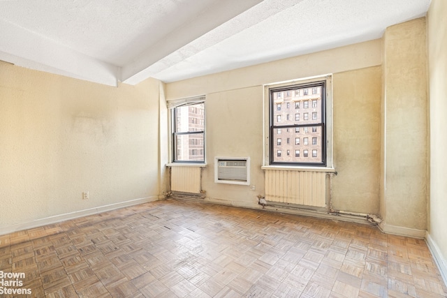 spare room with radiator, a textured ceiling, baseboards, and an AC wall unit