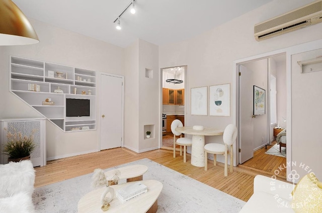 living room with a wall mounted air conditioner, wood finished floors, and rail lighting