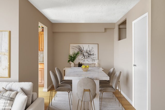 dining room featuring light wood-style floors, a textured ceiling, and baseboards