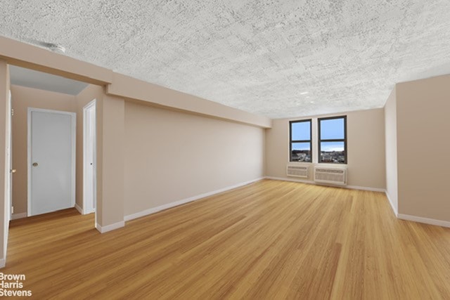 empty room with baseboards, a wall unit AC, light wood-style flooring, and a textured ceiling