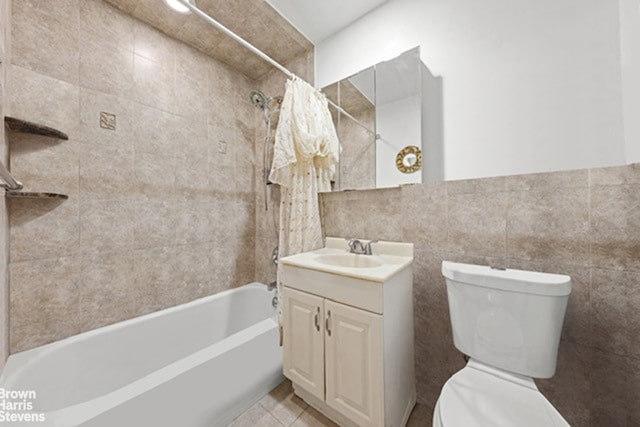 full bathroom with tile walls, shower / bathtub combination with curtain, toilet, vanity, and tile patterned floors