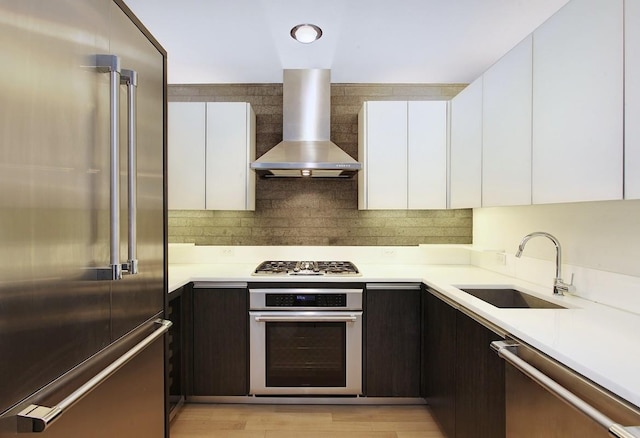 kitchen with a sink, light countertops, appliances with stainless steel finishes, white cabinetry, and wall chimney exhaust hood