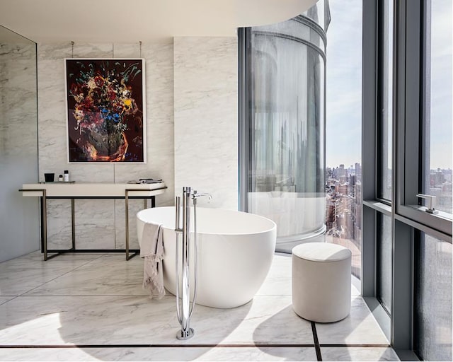 full bath with marble finish floor, a soaking tub, tile walls, and a city view