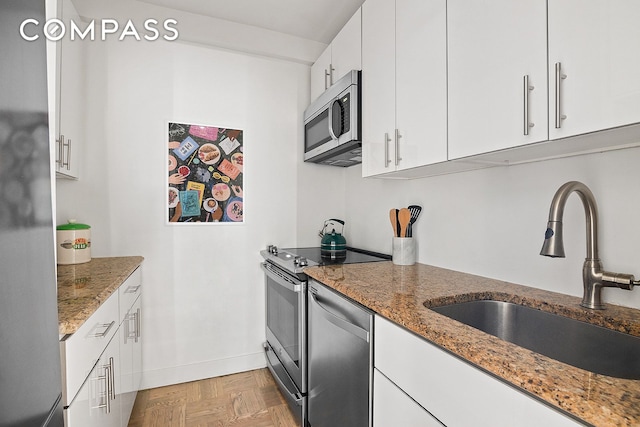 kitchen with a sink, light stone counters, white cabinetry, appliances with stainless steel finishes, and baseboards