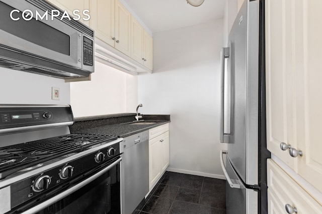 kitchen featuring stainless steel appliances, dark countertops, a sink, dark tile patterned floors, and baseboards