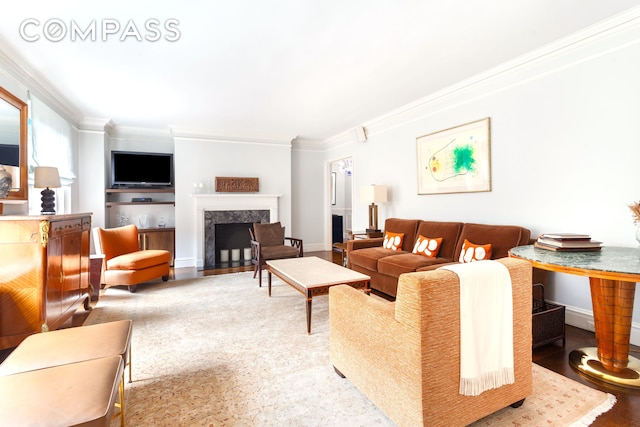 living area with ornamental molding, a premium fireplace, wood finished floors, and baseboards